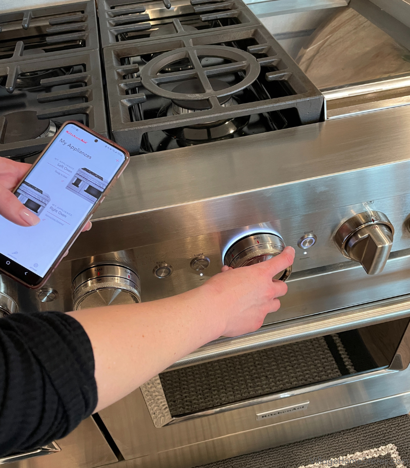 stainless steel kitchenaid range with hand holding iphone open to the kitchenaid app connecting to the range